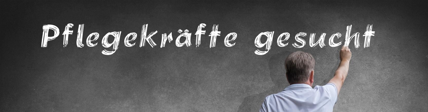 Mann schreibt mit Kreide "Pflegekräfte gesucht an die Tafel"