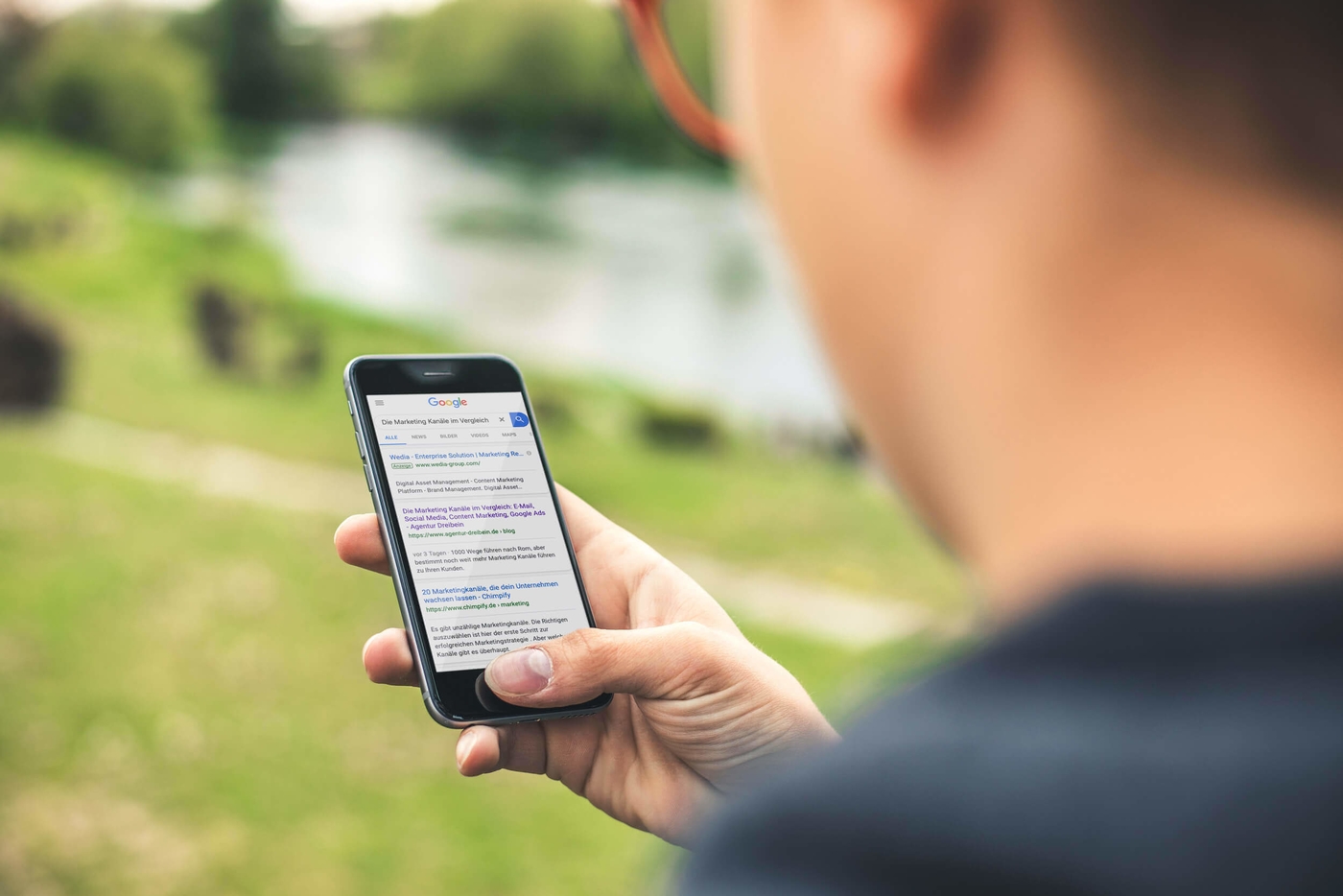 Mann googlet mit dem Smartphone: Marketing Kanäle im Vergleich